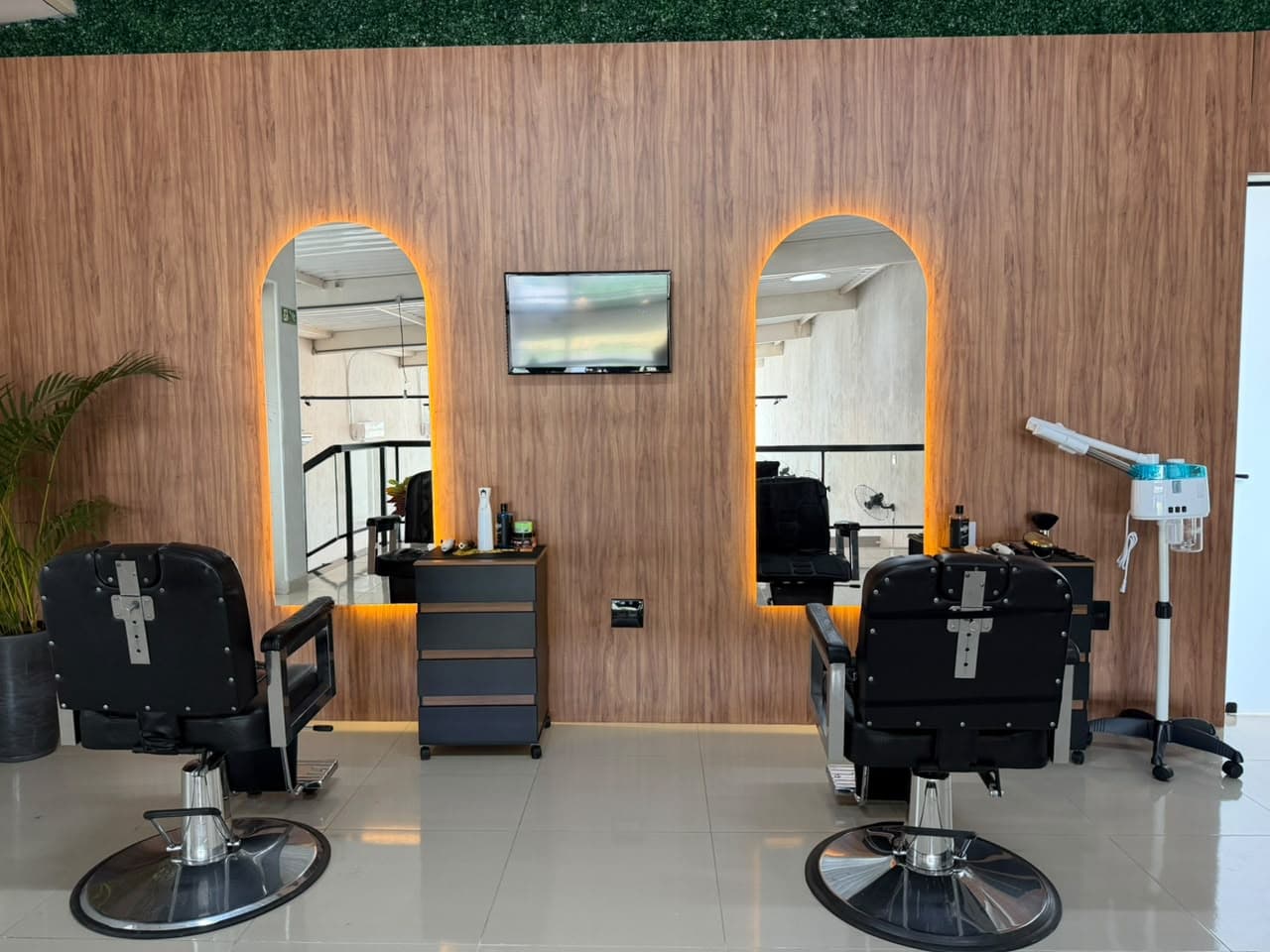 Ambiente da Impacto Barber Club: duas cadeiras e espelhos com luz dourada na parede de madeira